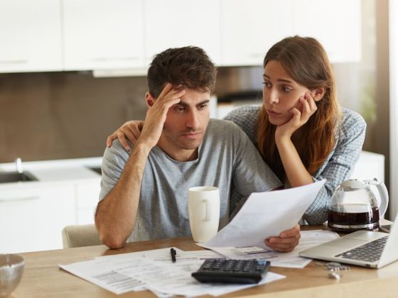 Casal analisa dívida antiga em documentos e notebook na mesa da cozinha