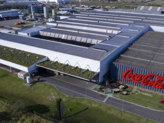 Vista aérea da maior fábrica da Coca-Cola do mundo, com galpão industrial de grande porte e logotipo da marca na fachada