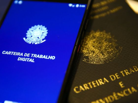 Carteira de trabalho digital e física sobre teclado de computador; IBGE divulga salário médio por estado em 2024