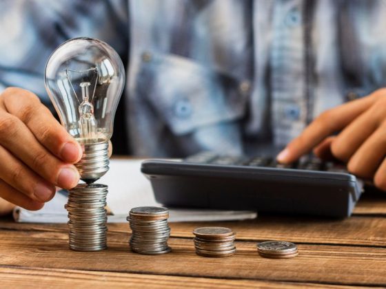 Pessoa segura lâmpada sobre pilhas de moedas ao lado de calculadora, ilustrando desconto na conta de luz