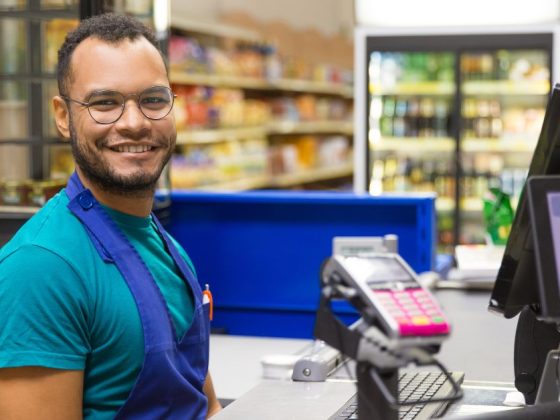 Funcionário de supermercado sorrindo no caixa após fim da escala 6x1