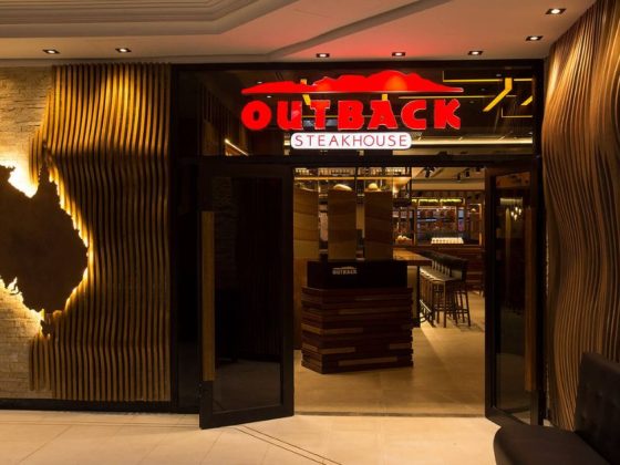 Fachada de restaurante Outback Steakhouse com letreiro iluminado e mapa da Austrália na parede; Outback em Montes Claros abre neste domingo