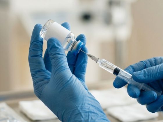 Anvisa proíbe antibiótico: mãos com luvas cirúrgicas preparam medicamento injetável com seringa em ambiente hospitalar