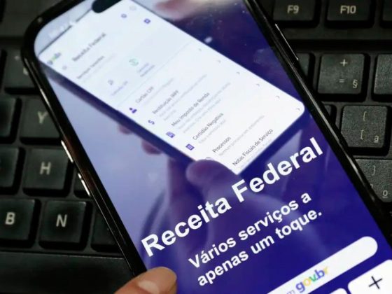 Mão segura celular com aplicativo da Receita Federal aberto para consulta ao cashback do IR