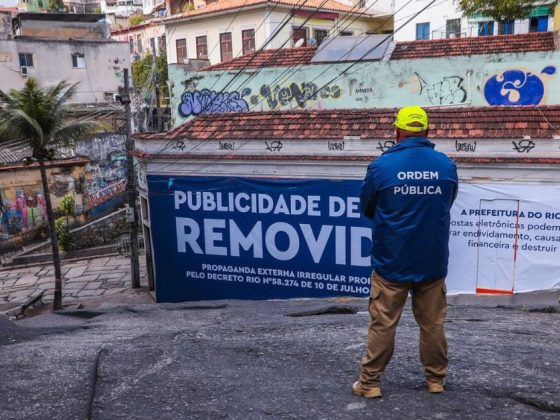 Agente de ordem pública diante de banner de remoção de publicidade irregular de bets no Rio de Janeiro, com alertas em anúncios de bets afixados pela prefeitura.