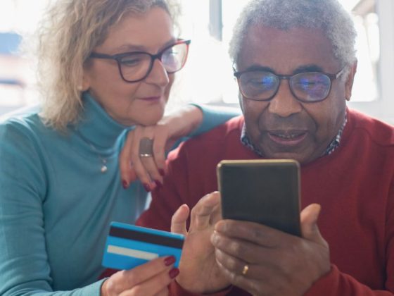 casal de idosos consultando transações financeiras de idosos pelo celular com cartão na mão