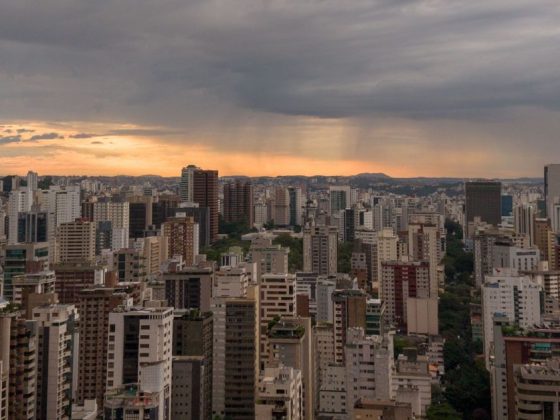 Vista aérea de Belo Horizonte com céu nublado e chuva ao fundo ilustra a previsão do tempo em BH