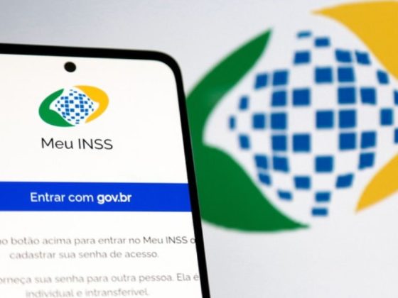 Aplicativo Meu INSS em agosto aberto em celular com logo da Previdência Social ao fundo