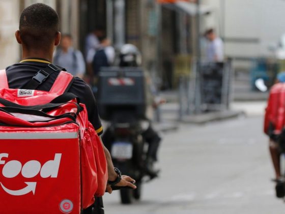Alt text Motoristas de aplicativo em via urbana, com mochila térmica do iFood em destaque