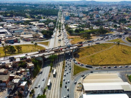 Vista aérea do Anel Rodoviário de BH, com trânsito intenso de carros e caminhões nas pistas marginais e viaduto ao fundo