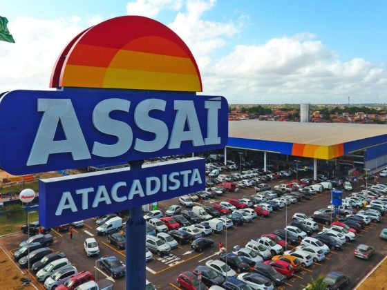 Placa e fachada do Assaí Atacadista com estacionamento lotado; rede inaugura farmácia do Assaí em julho
