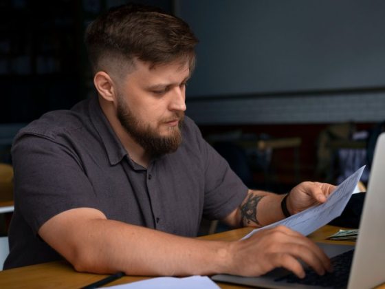 homem analisa desconto no IPTU em documento com notebook aberto à frente