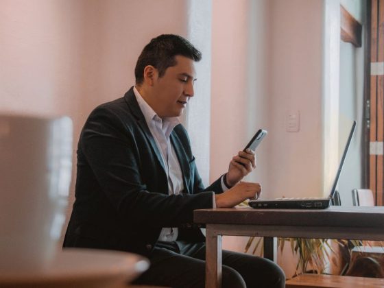 Homem empreendedor consulta Desenrola 2.0 no celular ao lado de notebook