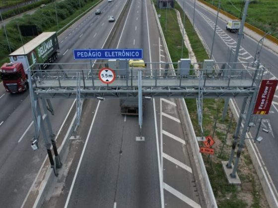 Pórtico de free flow em rodovia com placa de pedágio eletrônico e veículos em movimento