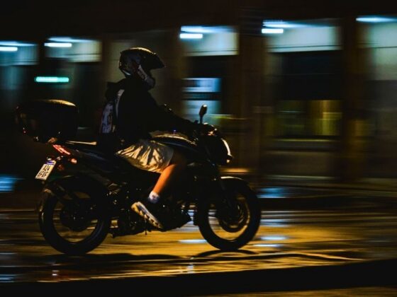 Motoboy em moto com baú percorre rua molhada à noite em área urbana