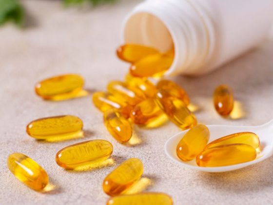 Cápsulas de suplementos Newfit derramadas de um pote sobre a mesa, ao lado de uma colher.