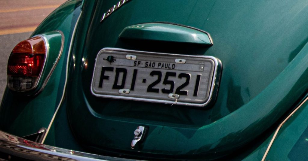 Placa padrão cinza antiga com identificação de cidade e estado em Fusca verde.