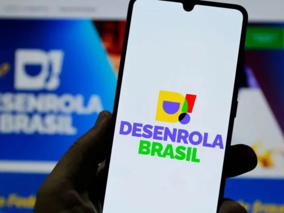 Tela de celular exibindo o logo do Novo Desenrola Brasil com site do programa ao fundo