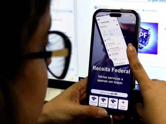Mulher segura celular com aplicativo da Receita Federal aberto para consultar a restituição do Imposto de Renda 2026