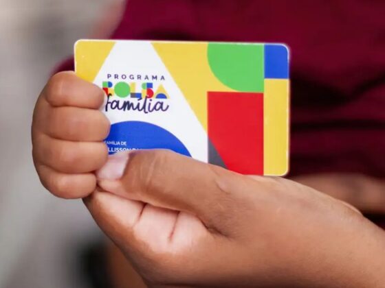 Mão segurando cartão do Bolsa Família de setembro com logo colorida do programa