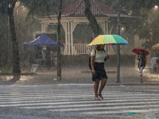 Pedestres atravessam faixa sob chuva intensa com guarda-chuvas coloridos; risco geológico em BH foi ampliado pela Defesa Civil nesta terça (15)