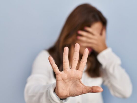 Mulher cobre o rosto e estende a mão em gesto de recusa, representando afastamento remunerado por violência doméstica