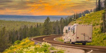 Camper Driving Down Road in The Beautiful Countryside Among Pine Trees and Flowers.