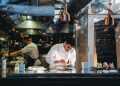 A chef is cooking in his restaurant's kitchen. Shot through the glass. High-end gourmet restaurant.