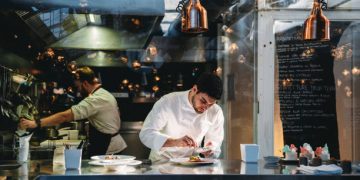 A chef is cooking in his restaurant's kitchen. Shot through the glass. High-end gourmet restaurant.