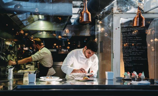A chef is cooking in his restaurant's kitchen. Shot through the glass. High-end gourmet restaurant.