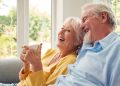 Retired Senior Couple Sitting On Sofa At Home Drinking Coffee And Watching TV Together