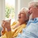 Retired Senior Couple Sitting On Sofa At Home Drinking Coffee And Watching TV Together