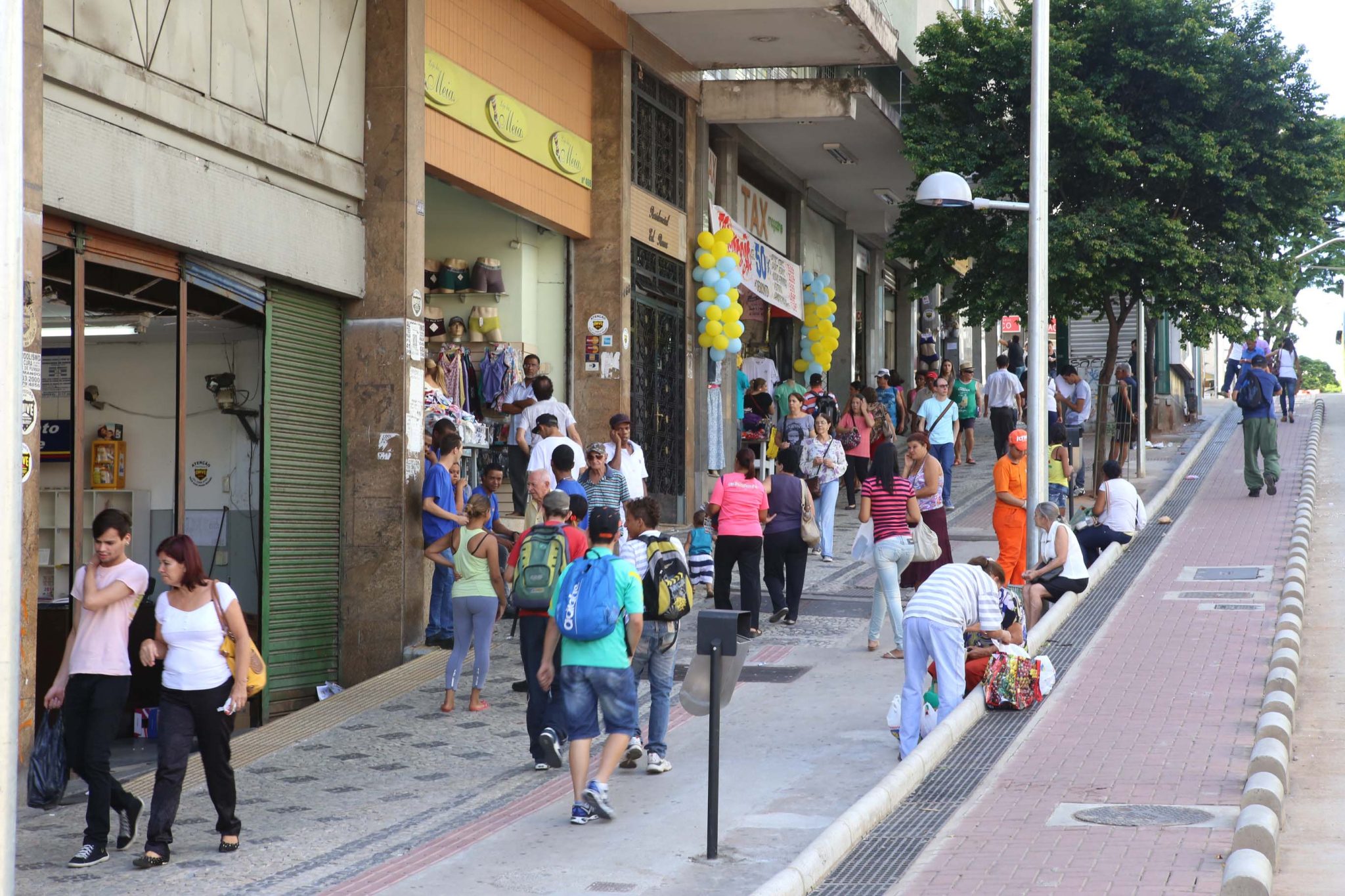 Pessoas andam em rua de Belo Horizonte e passam por vários estabelecimentos comerciais