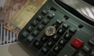 Na foto vemos uma moeda de um real, uma calculadora e notas de dez reais