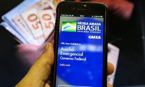 Aplicativo do auxílio emergencial aberto em celular. Ao fundo várias notas de cinquenta reais