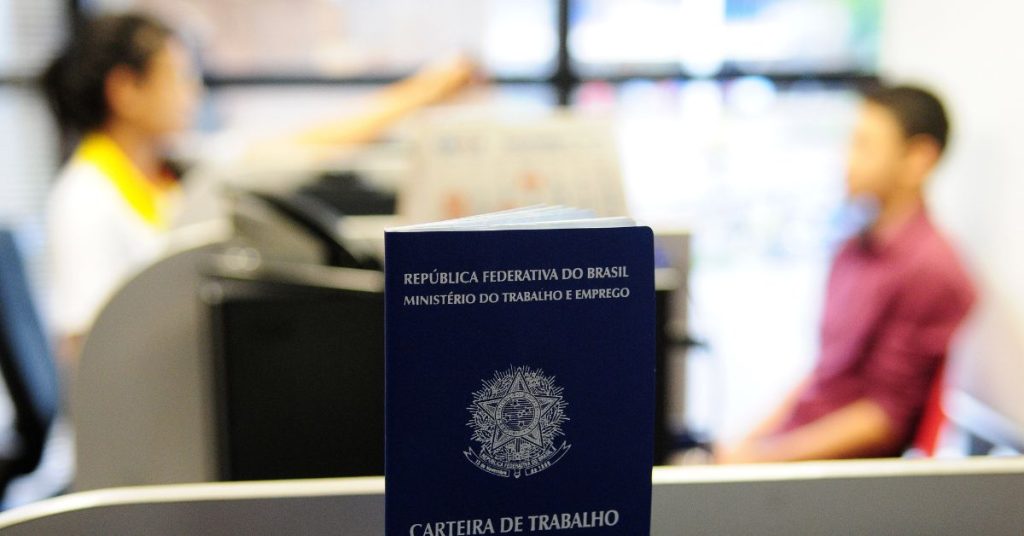 Imagem de uma Carteira de Trabalho com uma entrevista de emprego ao fundo