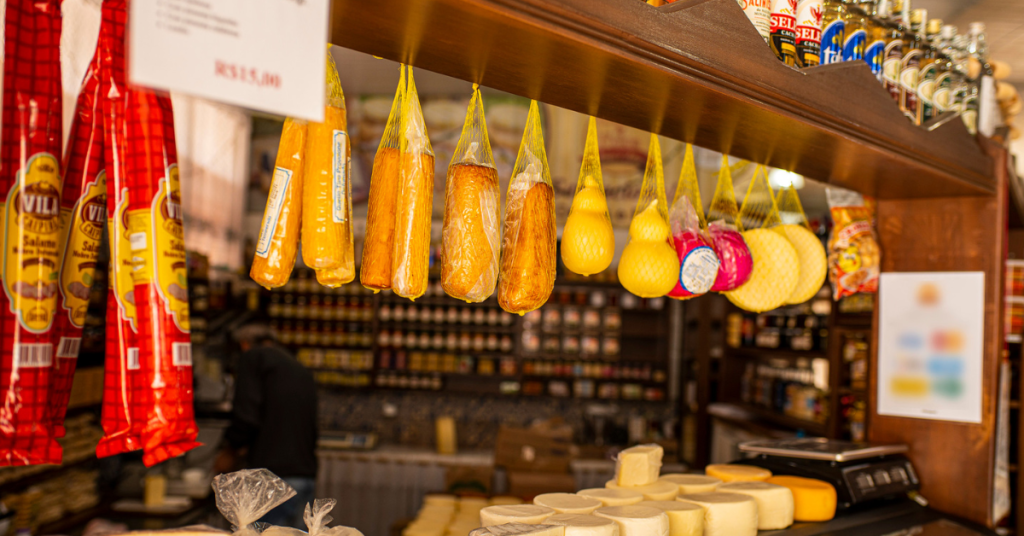 Imagem de feira de alimentos em São Lourenço, Minas Gerais, com foco em uma barraca onde estão expostos produtos típicos como queijos e cachaças. 