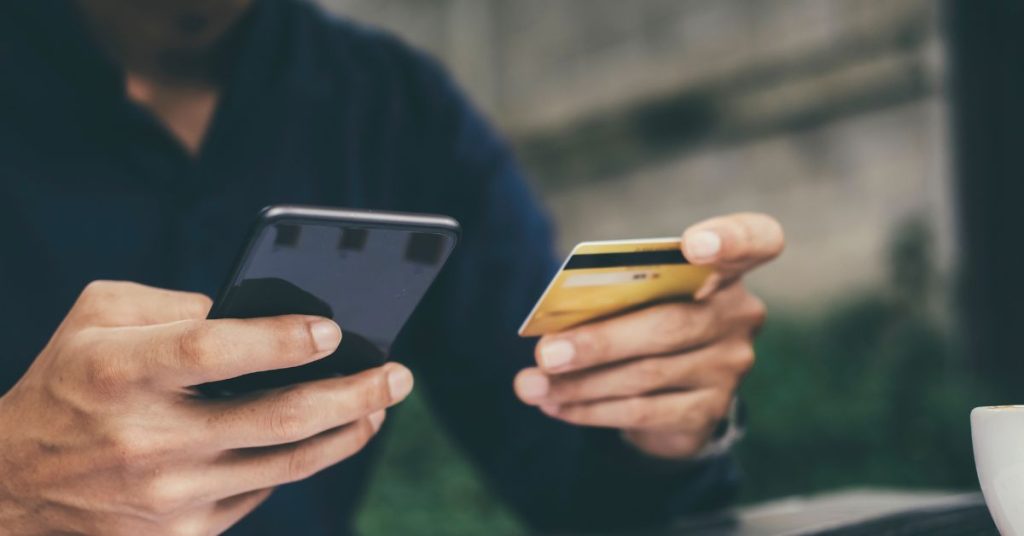 Homem segurando um celular e um cartão de crédito.