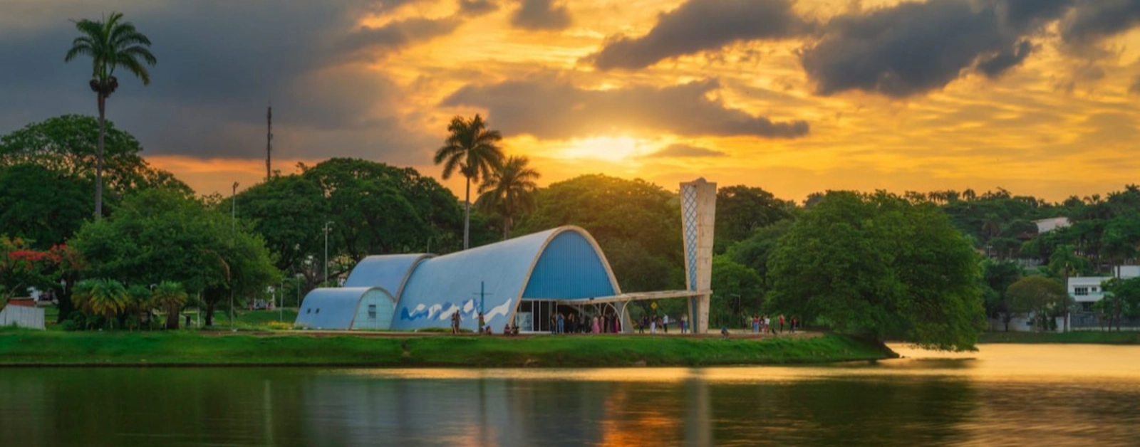 Igreja da Pampulha ao pôr do sol com lago e céu laranja vibrante.