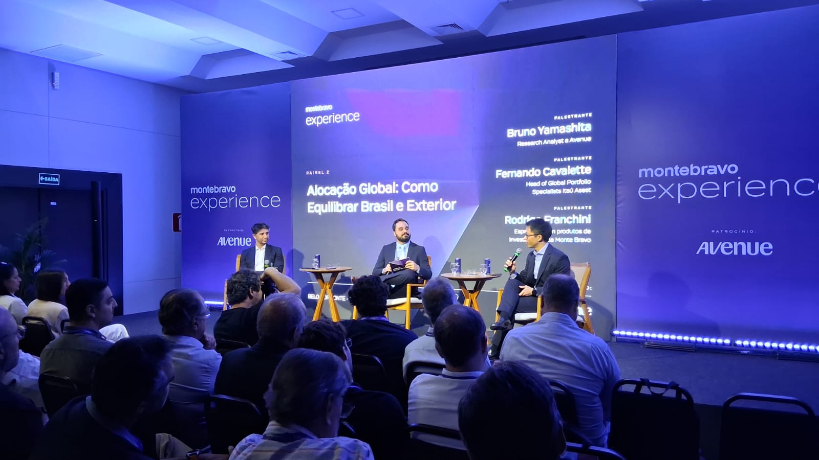 Painel de discussão sobre alocação global de investimentos com palestrantes e plateia atenta.