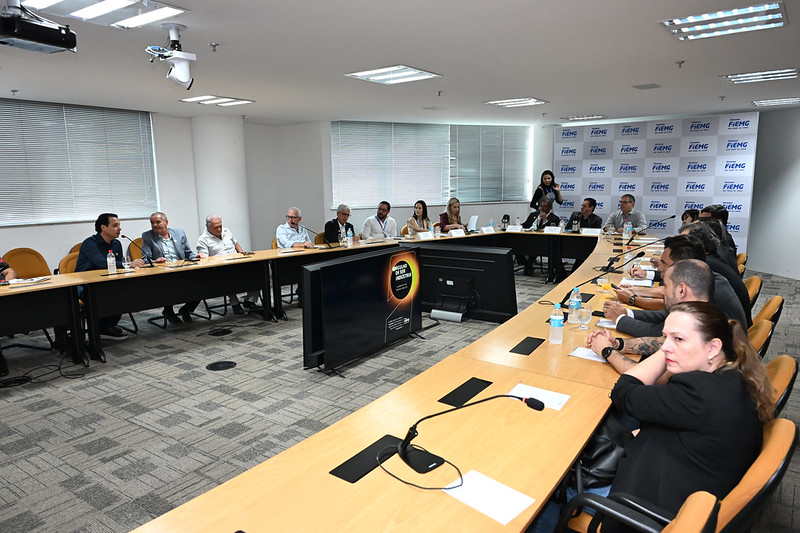 Reunião de negócios em sala moderna com diversas pessoas ao redor de mesa em formato de U.