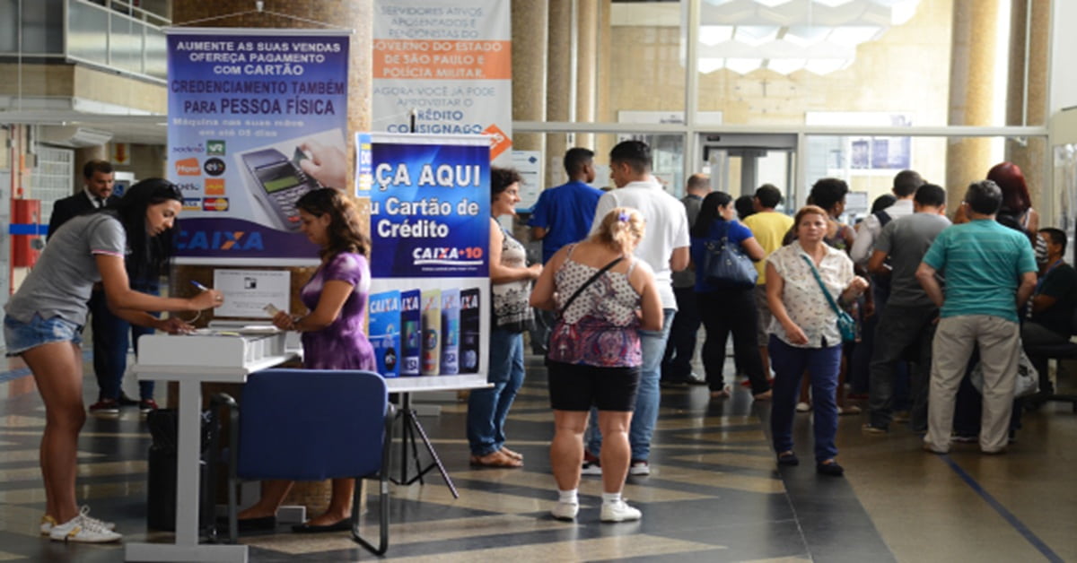 Pessoas aguardando atendimento, em pé, na porta de entrada de um banco