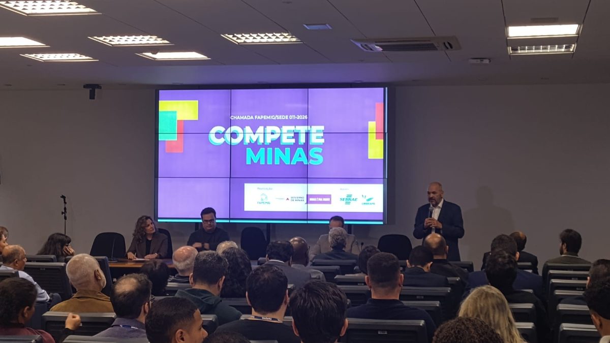 Auditório cheio com um telão à frente da plateia com os dizeres Compete Minas