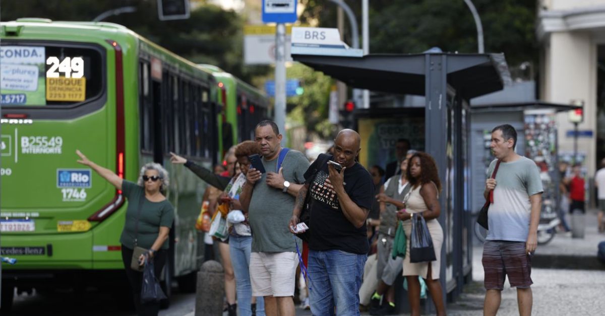 Pessoas aguardando e embarcando em um ônibus verde em uma parada de transporte público.