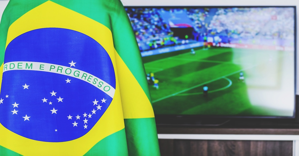 Bandeira do Brasil em destaque. Ao fundo um aparelho televisor