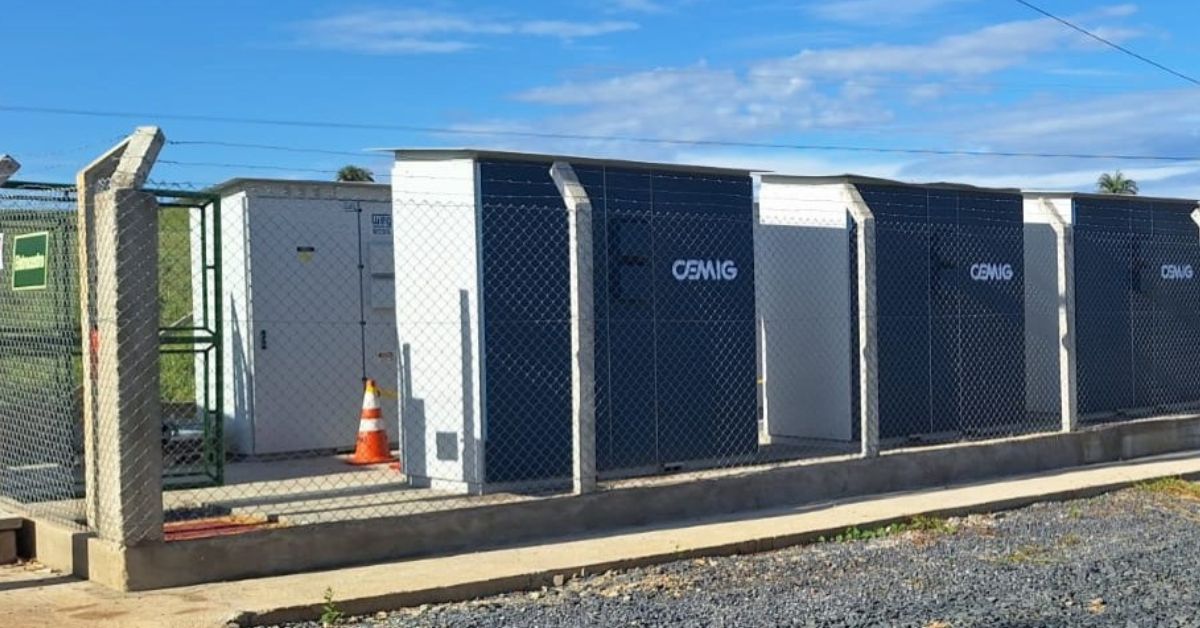 Sistema de armazenamento de energia em baterias da Cemig instalado em área cercada. Os módulos, utilizados para estocar energia gerada por fontes renováveis, estão alinhados em estrutura externa sob céu azul, em unidade voltada à segurança e à eficiência energética.