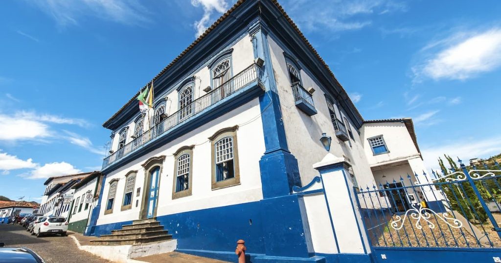 Casarão histórico com paredes brancas e detalhes em azul sob céu azul.