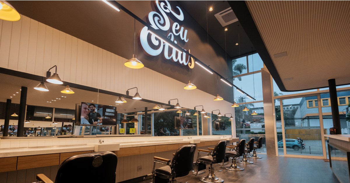 Imagem de uma barbearia com várias cadeiras dispostas e espelho amplo