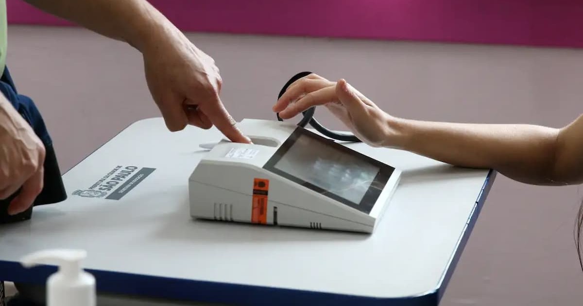 Pessoa coloca o dedo no leitor biométrico de uma urna eletrônica para identificação.
