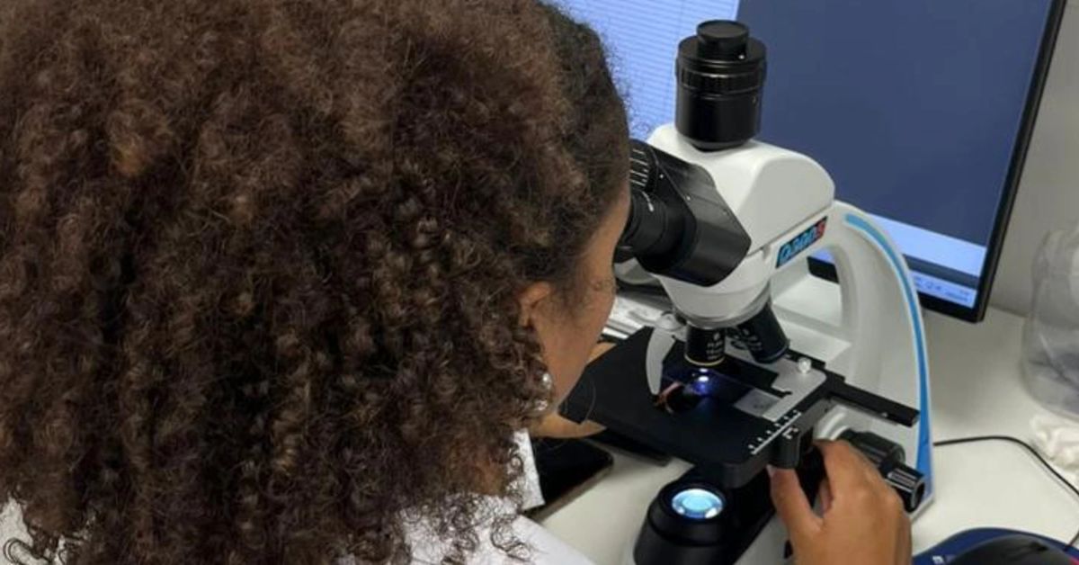 Pesquisadora trabalhando com microscópio óptico conectada a um monitor de computador.
